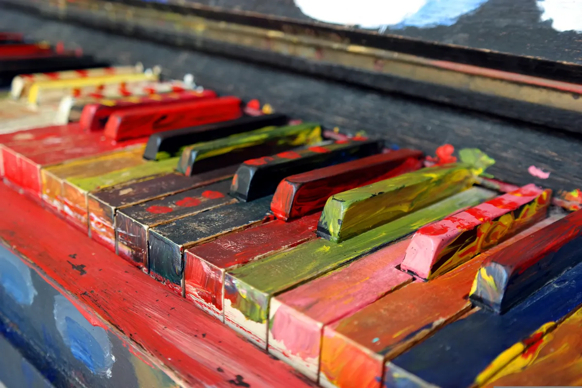 Closeup photograph of piano keys; the keys have been colorfully (and roughly) painted, with brush strokes and paint layering visible. All of the keys look weathered.
