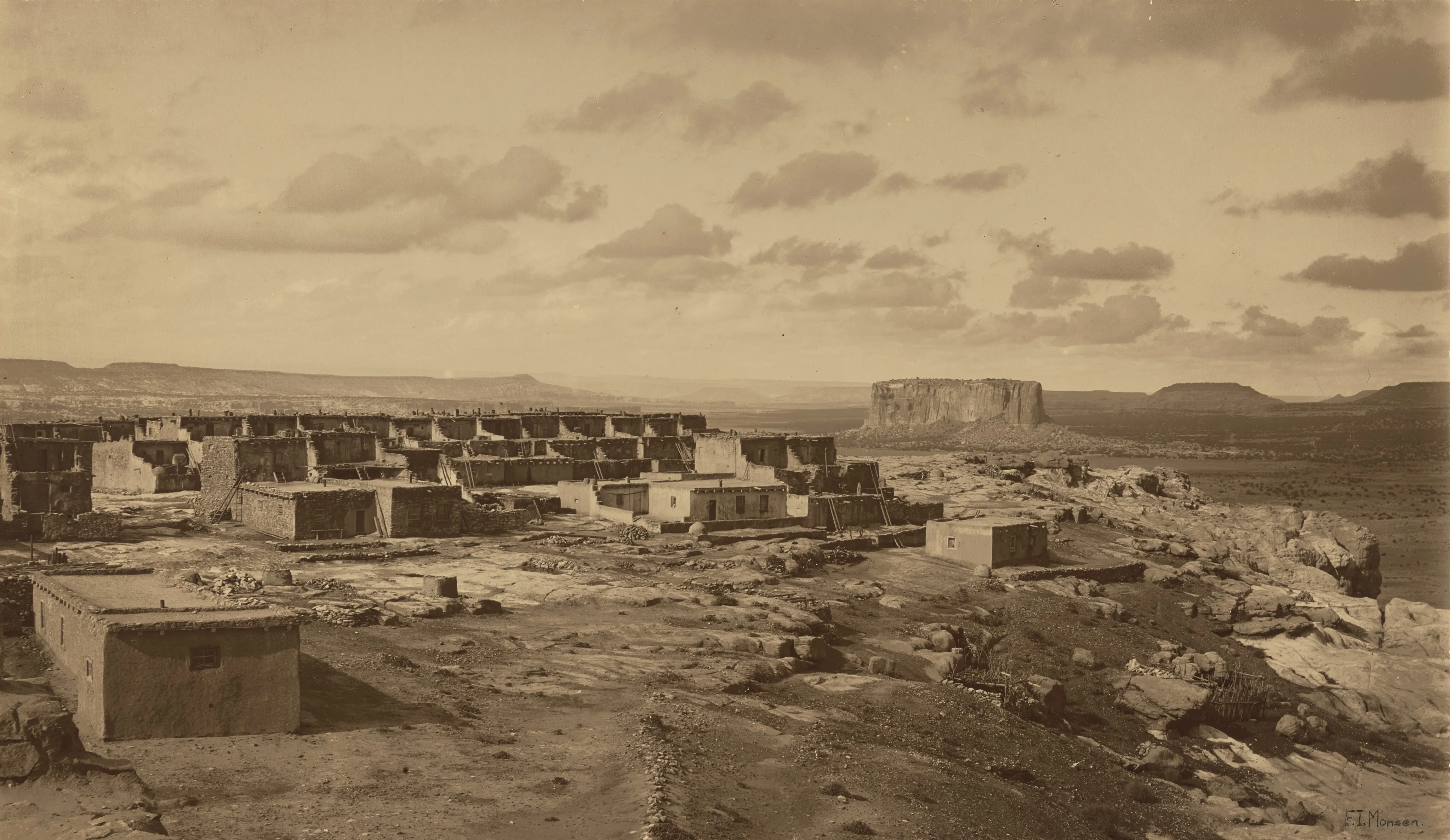 Monochrome photograph of pueblo ruins in a desert mesa landscape. The image has a brownish cast and is rather dreamlike.