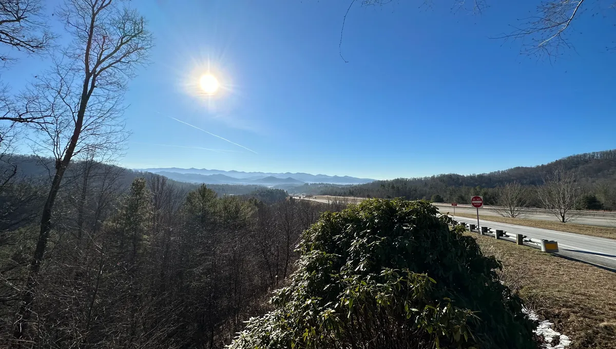 Frosty morning a few days after Christmas. On the right side, a road curves to the left and runs into the distance; it runs alongside a ravine covered in small trees with no leaves on them. Mountains are visible in the distance, the ridges definded by low-lying fog.