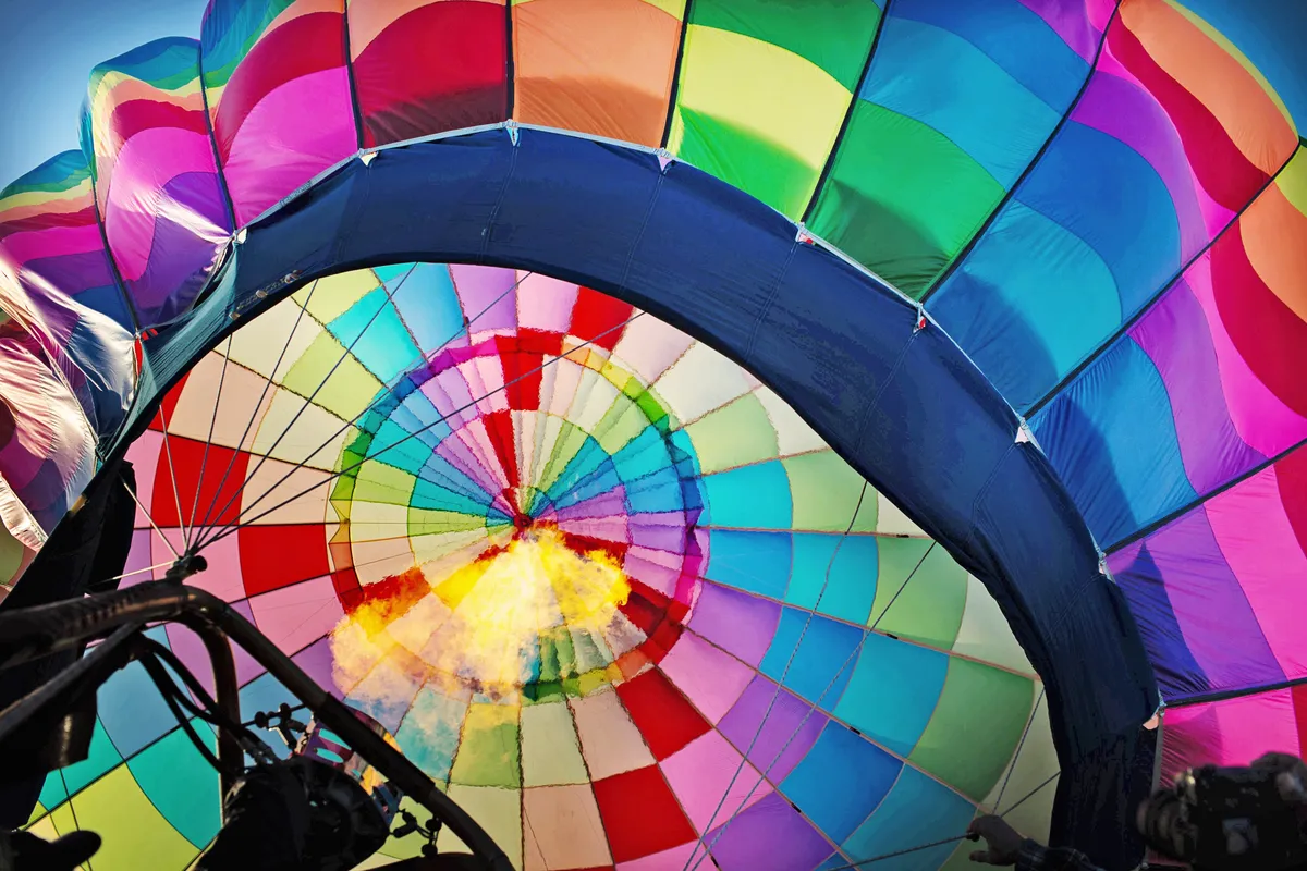 View from underneath an inflating hot air balloon. The balloon has a rainbow pattern, and you can see a jet of flame coming out of the burner.