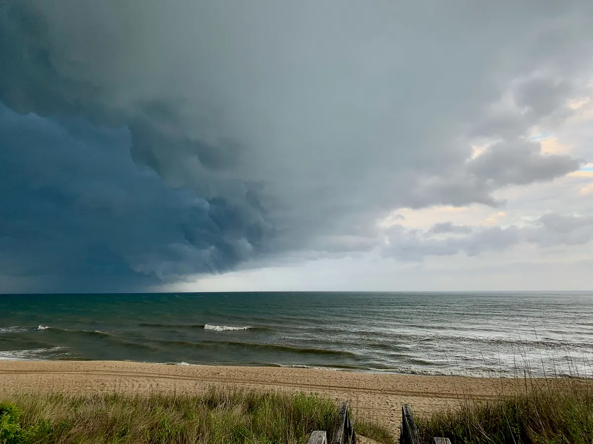 Beach scene at the outer banks; storm clouds rolling in from the North, with a bright sky on the right side and dark, threatening clouds on the left.